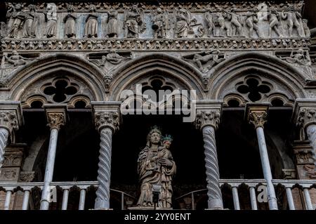 Statue der gekrönten Jungfrau und des Kindes von 1427 von Christoforo da Firenze, Westfront der Kathedrale St. Georg (Duomo di San Giorgio Martyre) in Ferrara, Emilia-Romagna, Italien. Die Statue befindet sich in einer Loggia, die in den 1200er Jahren hinzugefügt wurde und wird von zwei Spiralsäulen der Loggia mit Blätterkapitellen flankiert, die Bögen stützen, die von Vierfachfolien durchbrochen wurden. Auf dem Gipfel der Loggia befinden sich Szenen des letzten Jüngsten Gerichts, die in den 1200er Jahren von einem unbekannten Bildhauer im gotischen Stil gemeißelt wurden; dazu gehören das gerettete Rauschen aus ihren Särgen (über den Bögen) und das am Hals angekettete Verdammte (oben rechts). Stockfoto