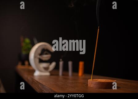 Räucherstäbchen raucht auf einem Holzständer auf dunklem Hintergrund. Aromatherapie, Rauch beim Verbrennen von Weihrauch. Rauch für Gebete und Meditation. Beten zu Stockfoto