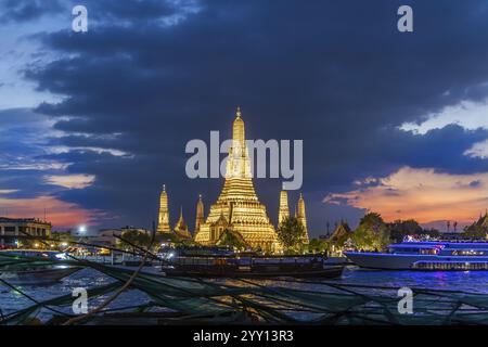 Wat Arun, Tempel der Dämmerung bei Sonnenuntergang mit dunklen Wolken. Boote auf dem Fluss Chao Phraya. Touristenattraktion in Bangkok, Thailand, Asien Stockfoto