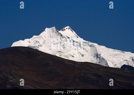 Boliviens majestätischer Berg Huayna Potosí in Bolivien mit seinem schneebedeckten Gipfel, der vor einem dramatisch bewölkten Himmel steht. Stockfoto