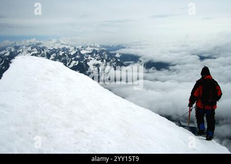 Der Kletterer steht auf dem Gipfel des Huayna Potosi und bietet einen atemberaubenden Blick auf schneebedeckte Gipfel und ein Wolkenmeer in Bolivien. Stockfoto