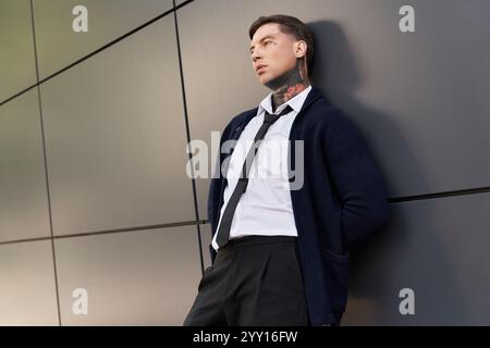 Hübscher junger Mann mit Tattoos in formeller Kleidung lehnt sich lässig an eine elegante Wand. Stockfoto