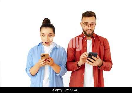 Überraschte Männer und Frauen reagieren auf etwas auf ihrem Smartphone, zeigen Aufregung oder Schock, tragen Freizeitkleidung, stehen auf einem isolierten weißen Hintergrund Stockfoto