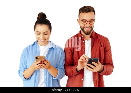 Lächelnder, fröhlicher Mann und Frau, die ihre Smartphones überprüfen, Online-Interaktionen genießen oder surfen, lässige Kleidung tragen und auf einem isolierten weißen Hintergrund stehen Stockfoto