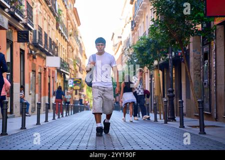 Junger Latino-Mann, der mit dem Rucksack die Straße der Stadt entlang läuft Stockfoto