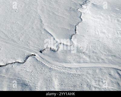 Luftaufnahme eines kleinen Baches, der sich in der verschneiten Landschaft des Hochhaedrich-Berggebietes im Bregenzer Wald in Vorarlberg, Österreich, windet Stockfoto