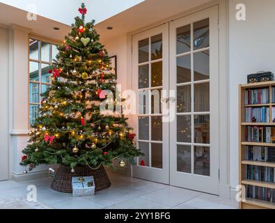 Inneneinrichtung mit geschmücktem Weihnachtsbaum und Geschenk unter dem Baum im Wohnzimmer Wintergarten, Großbritannien Stockfoto