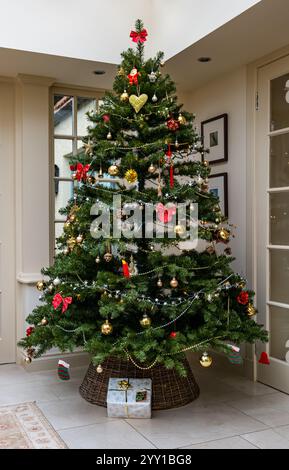 Inneneinrichtung mit geschmücktem Weihnachtsbaum und Geschenk unter dem Baum im Wohnzimmer Wintergarten, Großbritannien Stockfoto