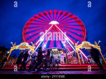 Schwerin, Deutschland. Dezember 2024. Besucher stehen vor einem Riesenrad auf dem Weihnachtsmarkt am Ufer des Pfaffenteichs. (Foto mit langer Belichtungszeit) in Mecklenburg-Vorpommern enden die meisten großen Weihnachtsmärkte wenige Tage vor Heiligabend - nur in Schwerin und Stralsund können die Glühweinstände und Mutzen-Stände noch nach den Feiertagen besucht werden. Der Schweriner Markt endet am 30. Dezember, der Stralsunder Markt endet erst im Dezember 31. Quelle: Jens Büttner/dpa/Alamy Live News Stockfoto