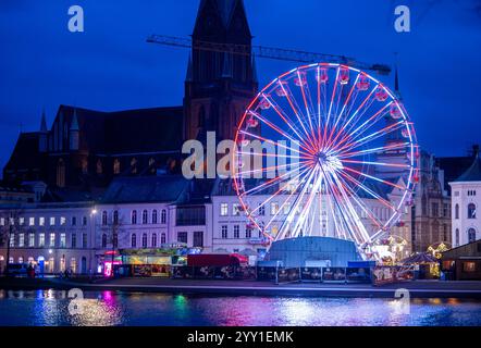 Schwerin, Deutschland. Dezember 2024. Ein Riesenrad dreht sich am Weihnachtsmarkt vor dem Schweriner Dom am Ufer des Pfaffenteichs. In Mecklenburg-Vorpommern enden die meisten großen Weihnachtsmärkte wenige Tage vor Heiligabend - nur in Schwerin und Stralsund können Sie nach den Feiertagen noch die Glühweinstände und Mutzen Stände besuchen. Der Schweriner Markt endet am 30. Dezember, der Stralsunder Markt endet erst im Dezember 31. Quelle: Jens Büttner/dpa/Alamy Live News Stockfoto