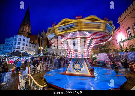 Schwerin, Deutschland. Dezember 2024. Am Weihnachtsmarkt vor der Kathedrale dreht sich ein Karussell. (Foto mit langer Belichtungszeit) in Mecklenburg-Vorpommern enden die meisten großen Weihnachtsmärkte wenige Tage vor Heiligabend - nur in Schwerin und Stralsund können die Glühweinstände und Mutzen-Stände noch nach den Feiertagen besucht werden. Der Schweriner Markt endet am 30. Dezember, der Stralsunder Markt endet erst im Dezember 31. Quelle: Jens Büttner/dpa/Alamy Live News Stockfoto