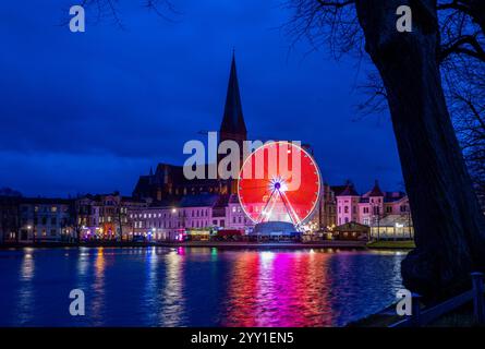 Schwerin, Deutschland. Dezember 2024. Ein Riesenrad dreht sich am Weihnachtsmarkt vor dem Schweriner Dom am Ufer des Pfaffenteichs. In Mecklenburg-Vorpommern enden die meisten großen Weihnachtsmärkte wenige Tage vor Heiligabend - nur in Schwerin und Stralsund können Sie nach den Feiertagen noch die Glühweinstände und Mutzen Stände besuchen. Der Schweriner Markt endet am 30. Dezember, der Stralsunder Markt endet erst im Dezember 31. Quelle: Jens Büttner/dpa/Alamy Live News Stockfoto