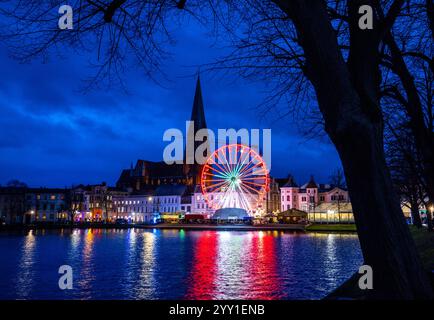 Schwerin, Deutschland. Dezember 2024. Ein Riesenrad dreht sich am Weihnachtsmarkt vor dem Schweriner Dom am Ufer des Pfaffenteichs. In Mecklenburg-Vorpommern enden die meisten großen Weihnachtsmärkte wenige Tage vor Heiligabend - nur in Schwerin und Stralsund können Sie nach den Feiertagen noch die Glühweinstände und Mutzen Stände besuchen. Der Schweriner Markt endet am 30. Dezember, der Stralsunder Markt endet erst im Dezember 31. Quelle: Jens Büttner/dpa/Alamy Live News Stockfoto