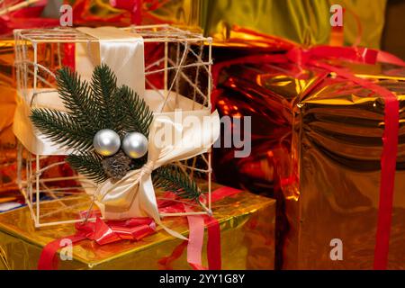 Hell gewickelte Geschenke in Gold und Rot schaffen eine festliche Atmosphäre, die mit einem dekorativen Geschenk mit Kiefer und Ornamenten verziert ist. Diese Anordnung c Stockfoto