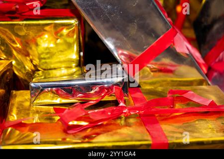 Eine Kollektion glänzender Geschenke in Gold und Silber, die mit roten Bändern gebunden sind, präsentiert ein festliches Arrangement, das ideal für Feiertage, Geburtstage oder besondere Veranstaltungen ist Stockfoto