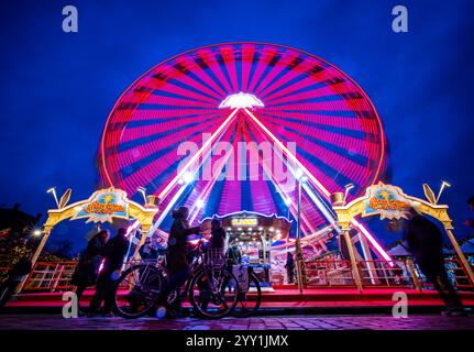 Schwerin, Deutschland. Dezember 2024. Besucher stehen vor einem Riesenrad auf dem Weihnachtsmarkt am Ufer des Pfaffenteichs. (Foto mit langer Belichtungszeit) in Mecklenburg-Vorpommern enden die meisten großen Weihnachtsmärkte wenige Tage vor Heiligabend - nur in Schwerin und Stralsund können Sie nach den Feiertagen noch Glühweinstand und Mutzenstand besuchen. In Schwerin endet der Markt am 30. Dezember. Quelle: Jens Büttner/dpa/Alamy Live News Stockfoto