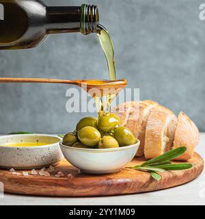 Gießen Sie Olivenöl in einen Löffel über grüne Oliven. Biologisches italienisches kaltgepresstes Olivenöl. Gesundes, mittelgrosses Lebensmittelkonzept. Stockfoto