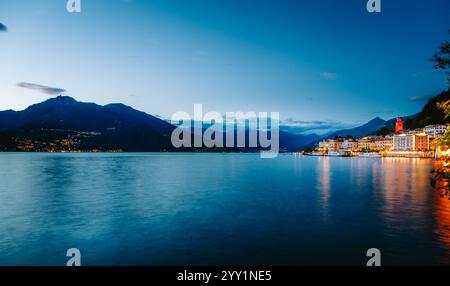 Ruhiges Wasser, das während der blauen Stunde die bezaubernden Lichter des Dorfes Bellagio am Comer See reflektiert, umgeben von einer atemberaubenden Bergkette in der Lombardei, Italien Stockfoto