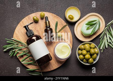 Olivenöl Hautpflegeprodukte mit Oliven und grünen Blättern auf dunkelbraunem Hintergrund, Draufsicht. Bio-Olivenöl für Gesicht oder Haarpflege, Öko-Spa-Kosmetik-Produkt Stockfoto