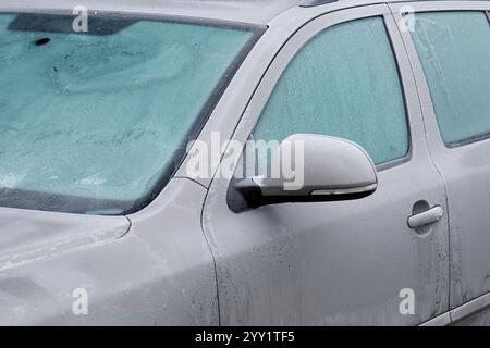 Gefrorene Fenster eines Autos an einem kalten Wintertag, Nahaufnahme eines grauen Autos mit Eiskristallen Stockfoto