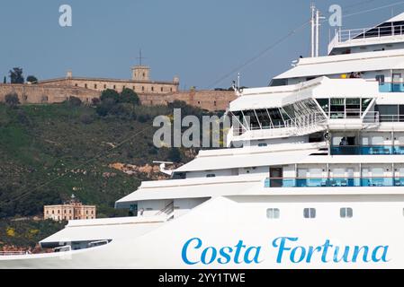 Nahaufnahme des Kreuzfahrtschiffs Costa Fortuna von Costa Cruises, im Hintergrund sehen Sie den Berg Montjuic mit seiner Burg und Leuchtturm. Stockfoto