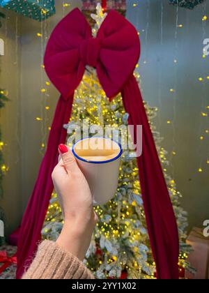 Das Bild zeigt eine festliche Winterszene im Innenbereich mit einem wunderschön beleuchteten Weihnachtsbaum, der mit hellen goldenen Feenlichtern und einem dramatischen Over verziert ist Stockfoto