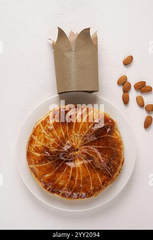 Französischer Königskuchen oder Galette des rois mit einer goldenen Krone, die auf einem weißen Teller und Hintergrund präsentiert wird, Draufsicht, Kopierraum Stockfoto