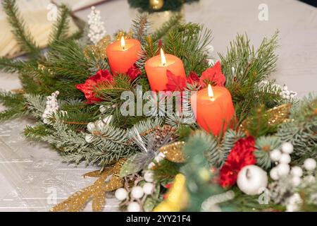 Erster Advent - geschmückter Adventskranz aus Tannenzweigen mit roten brennenden Kerzen auf einem Holztisch in der Zeit vor Weihnachten, festliches Bokeh im Stockfoto