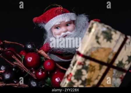 Kleiner weihnachtsmann versteckt sich hinter Mistel und weihnachtsgeschenk auf schwarzem Hintergrund, festliches Kartendesign mit dem heiligen nikolaus, Boxtag Stockfoto