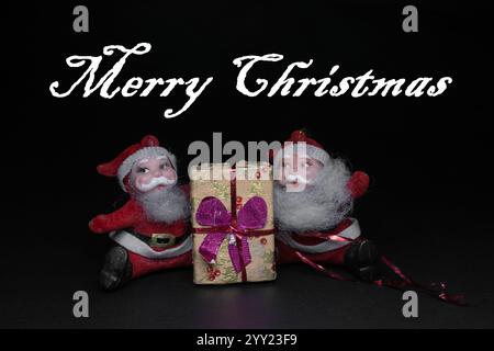 Vintage weihnachtsmann-Ornamente sitzen mit weihnachtsgeschenk auf dunklem Hintergrund mit MERRY CHRISTMAS Text Stockfoto