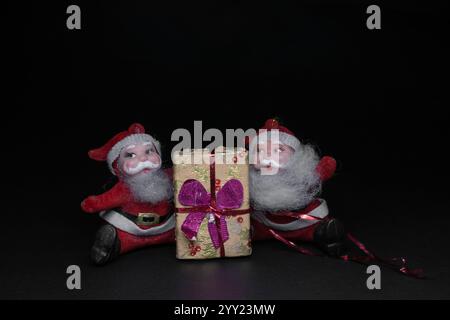 Vintage weihnachtsmann-Ornamente sitzen mit weihnachtsgeschenk auf dunklem Hintergrund mit Platz für Text Stockfoto