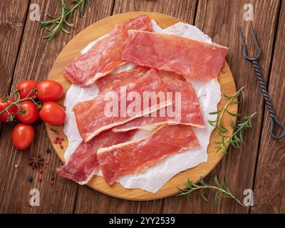 Blick von oben auf rohe geräucherte Schweinefleisch-Chips auf Holztablett mit Gemüse und Rosmarin auf dem Tisch, frisches Bier Stockfoto