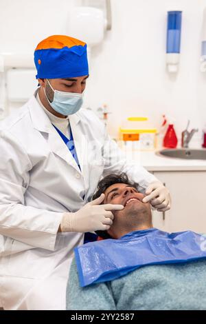 Zahnarzt mit Maske und Handschuhen, Untersuchung des Kiefers eines männlichen Patienten auf einem Zahnarztstuhl, umgeben von hellen und modernen Geräten in einer Welcom Stockfoto