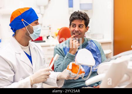 Zahnarzt mit Maske und Handschuhen zeigt einem Patienten, wie man mit einem Prothesenmodell und einer Zahnbürste während einer ärztlichen Untersuchung die Zähne richtig putzt i Stockfoto