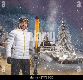 Männlicher Skier mit Ausrüstung stehend und in der Hand eines Paar Ski in einer verschneiten Nacht am Berg Stockfoto