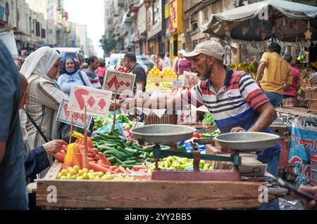 Ein lebhafter Straßenmarkt in Alexandria, Ägypten, auf dem frisches Gemüse, Waagen, Händler, und Einheimische, die täglich an Verkaufsständen einkaufen. Stockfoto