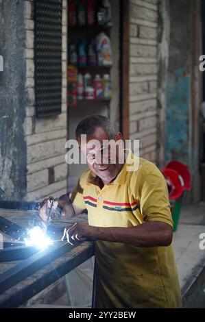 Ein Schweißer in Alexandria, Ägypten, arbeitet mit Funken, die fliegen, und trägt ein gelbes Hemd. Ein Einblick in handwerkliches Können in einer ägyptischen Werkstatt. Stockfoto