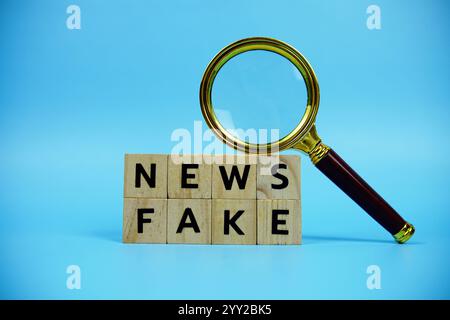 Fake News mit Holzblöcken Alphabetbuchstaben und Vergrößerungsglas auf blauem Hintergrund Stockfoto