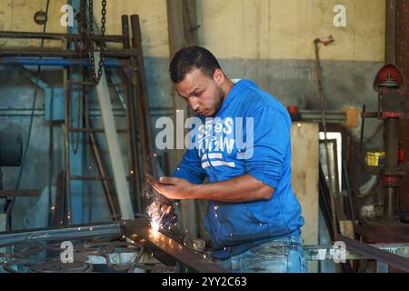 Junger ägyptischer Schweißer in Alexandria, der geschickt Metall schweißt, Funken fliegen. Eine lebendige Darstellung von Handwerkskunst und industrieller Arbeitskultur. Stockfoto