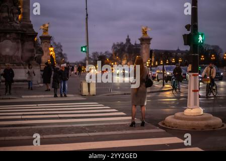 Während die Dämmerung die Landschaft verdunkelt, wartet eine junge attraktive Frau darauf, die Straße auf die Port Alexandre Brücke zu überqueren. Sie trägt einen klugen Anzug. Stockfoto