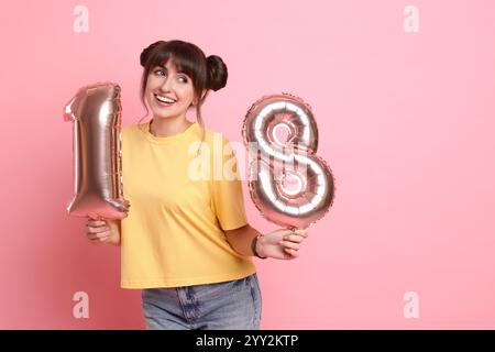 Coming of Age Party - 18. Geburtstag. Junge Frau, die nummernförmige Ballons auf rosa Hintergrund hält, Platz für Text Stockfoto