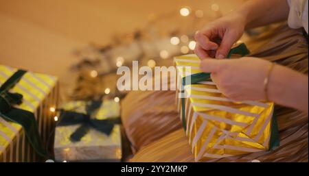 Nahaufnahme einer Frau, die ein goldenes Geschenk einpackt und ein Band bindet Stockfoto