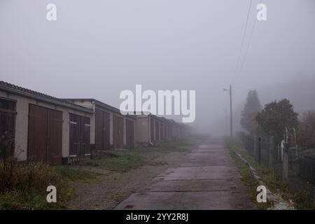 Herbst, nebeliger Morgen, Garagen und die Straße geht in die Ferne und verschwindet im Nebel. Stockfoto