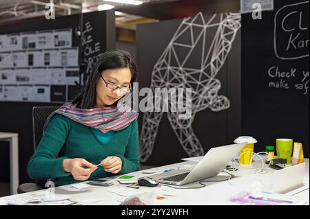 München, Bayern, Deutschland - 4. Februar. 2013: Eine Frau arbeitet an einem modernen Schreibtisch mit Laptop und Notizen in einem kreativ eingerichteten Büro. Die Umwelt Stockfoto