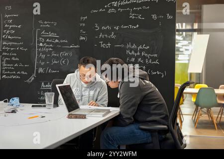 München, Bayern, Deutschland - 4. Februar. 2013: Zwei junge Männer in ungezwungener Kleidung arbeiten an einem weißen Tisch in einem modernen Büro. Stockfoto