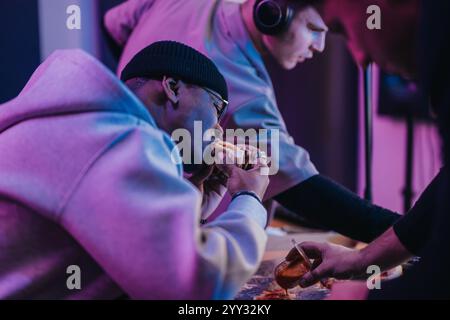 Eine Gruppe von Freunden, die während der Arbeit in einem Musikstudio einen verspielten Moment beim Essen verbringen. Stockfoto