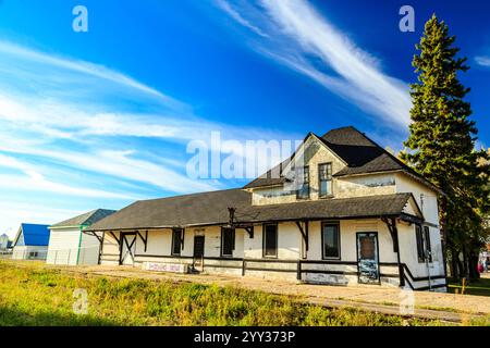 Ein großes weißes Haus mit einem schwarzen Dach liegt auf einem grasbewachsenen Feld. Das Haus ist von Bäumen umgeben und er wird verlassen. Der Himmel ist klar und blau, und der Stockfoto