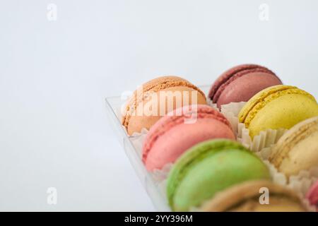 Französische Macarons mit weißer Paperpan in transparenter Plastikverpackung auf grauem Hintergrund, bunte Kuchen mit verschiedenen Geschmacksrichtungen. Appetitliches Dessert, Stockfoto