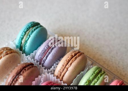 Helle französische Macarons mit weißer Papierpfanne, transparenter Plastikkarton auf Küchenarbeitsplatte, bunte Kuchen verschiedene Geschmacksrichtungen. Appetitlich Stockfoto