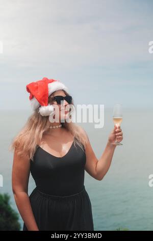 Porträt mit Frau in Sonnenbrille und Weihnachtsmann-Hut mit einem Glas Champagner Stockfoto